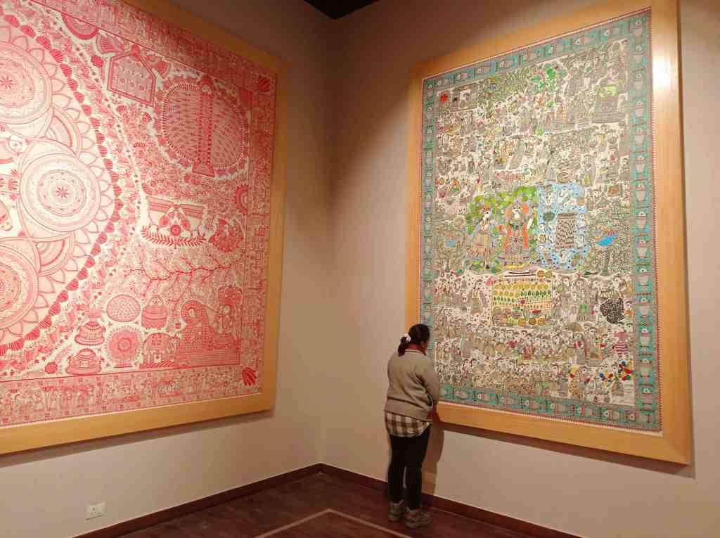A visitor observes two large, intricately designed wall hangings in the Bihar museum, one in shades of red and the other in vibrant colours, showcasing detailed motifs and patterns in Sujni art form.