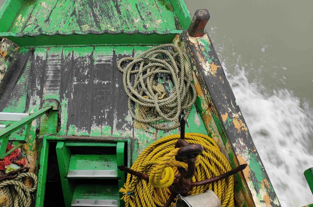Top view of a launch deck. It is green in colour and there is an anchor and yellow ropes kept. There is a flight of stairs that can be partially seen, going down
