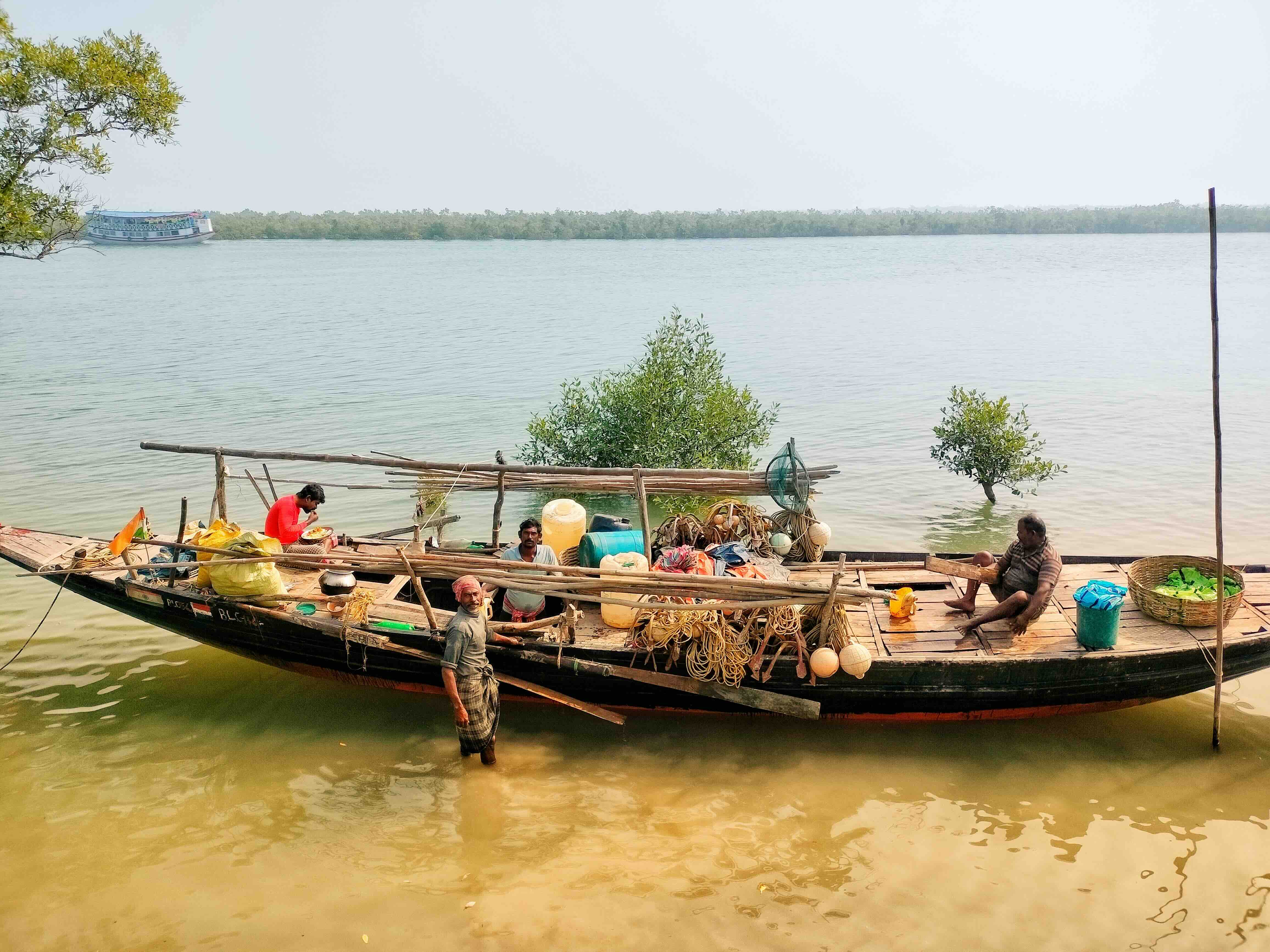 Men on and around a wooden boat filled with supplies on a calm river