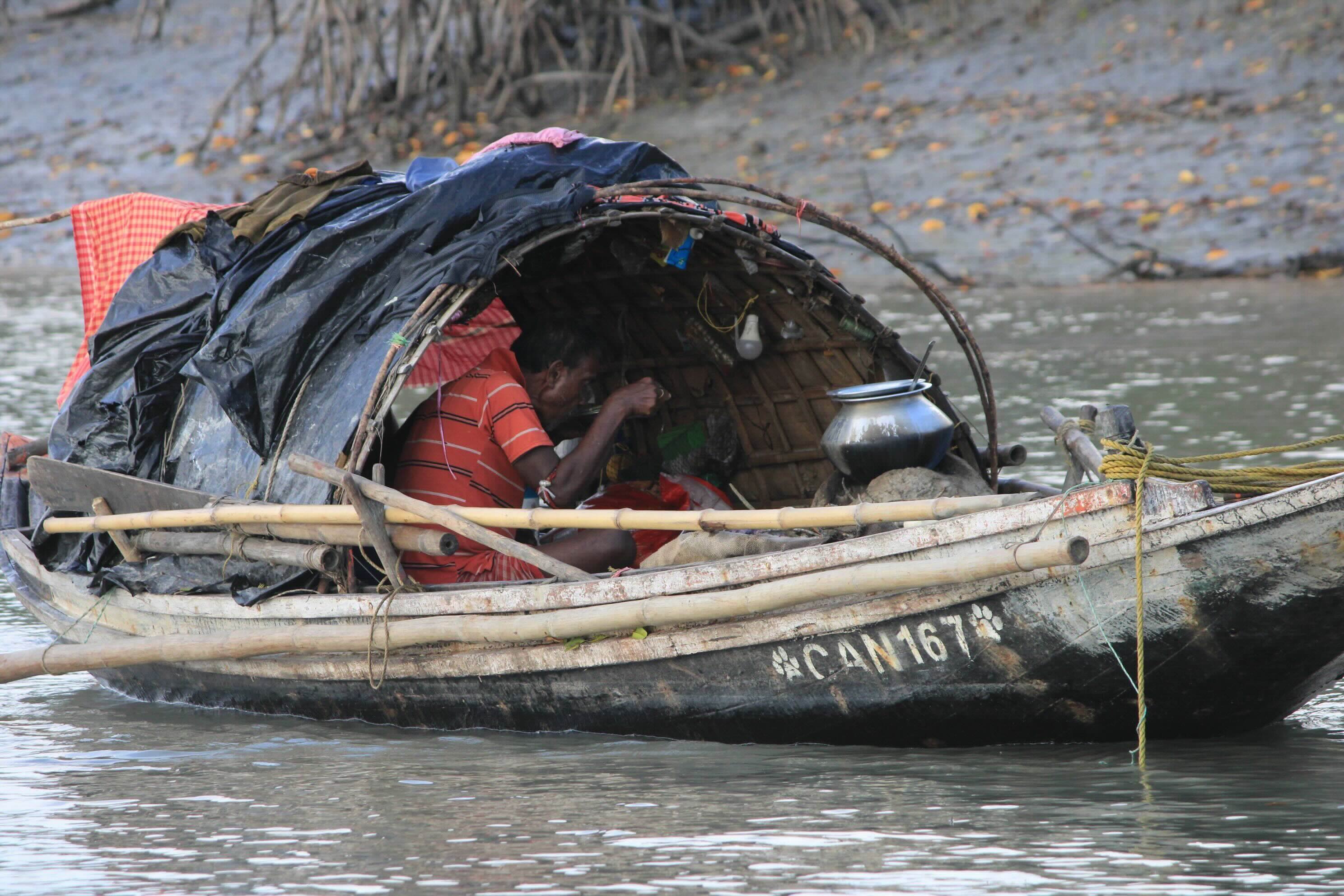 A man eats inside a small wooden boat marked CAN 167 on a river.