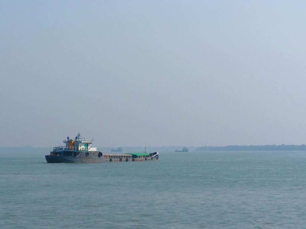A cargo ship moving across a wide, hazy body of water