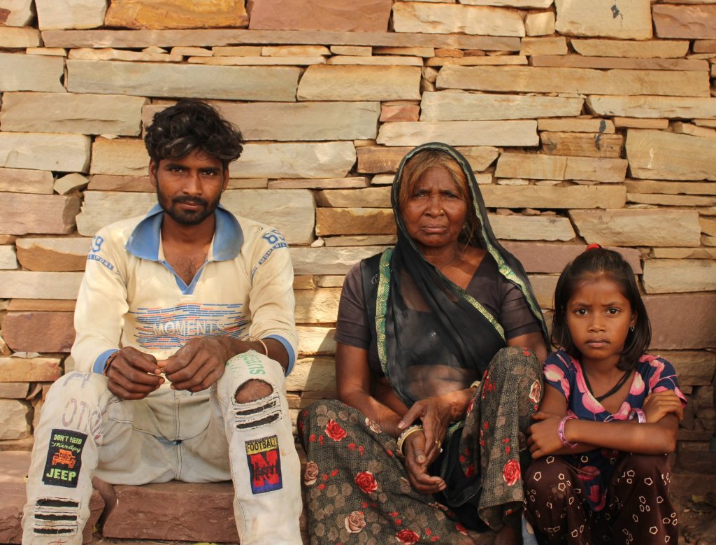 Man, older woman, and young girl sitting against a stone wall