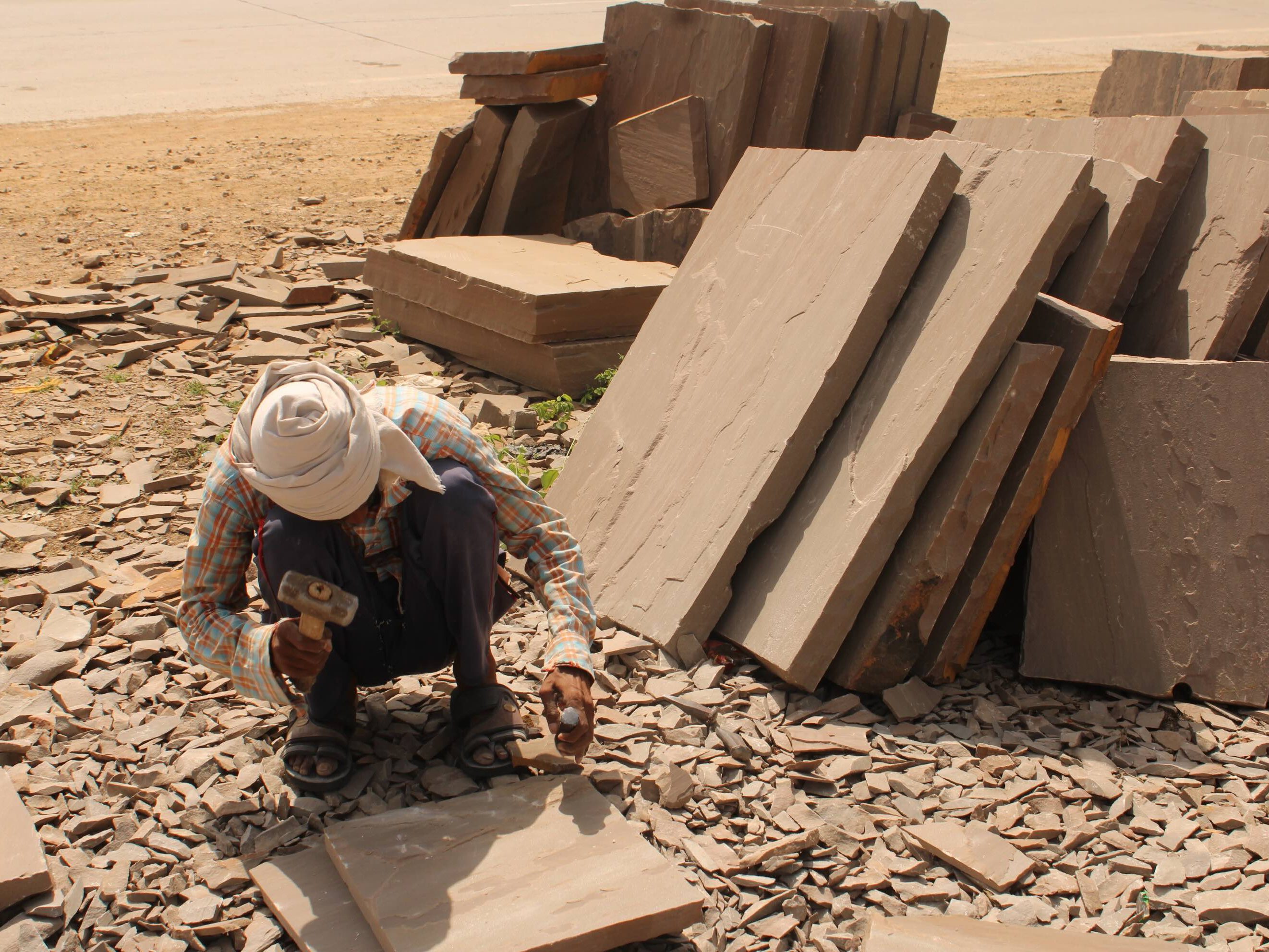 Worker shaping stone slabs surrounded by stacked stone pieces and debris