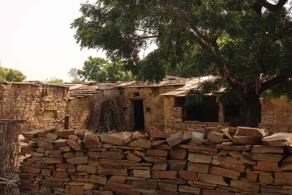 Old stone house with a wooden roof surrounded by stacked stones and greenery